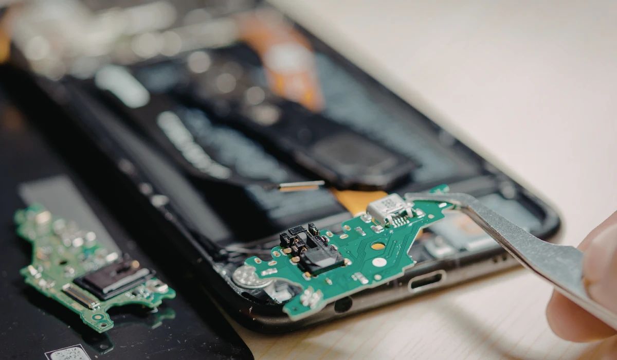 Técnico realizando microsoldadura en placa base bajo microscopio trinocular